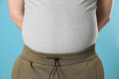 Photo of Overweight man in tight shirt on light blue background, closeup
