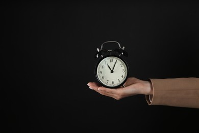 Photo of Businesswoman holding alarm clock on black background, closeup with space for text. Time management