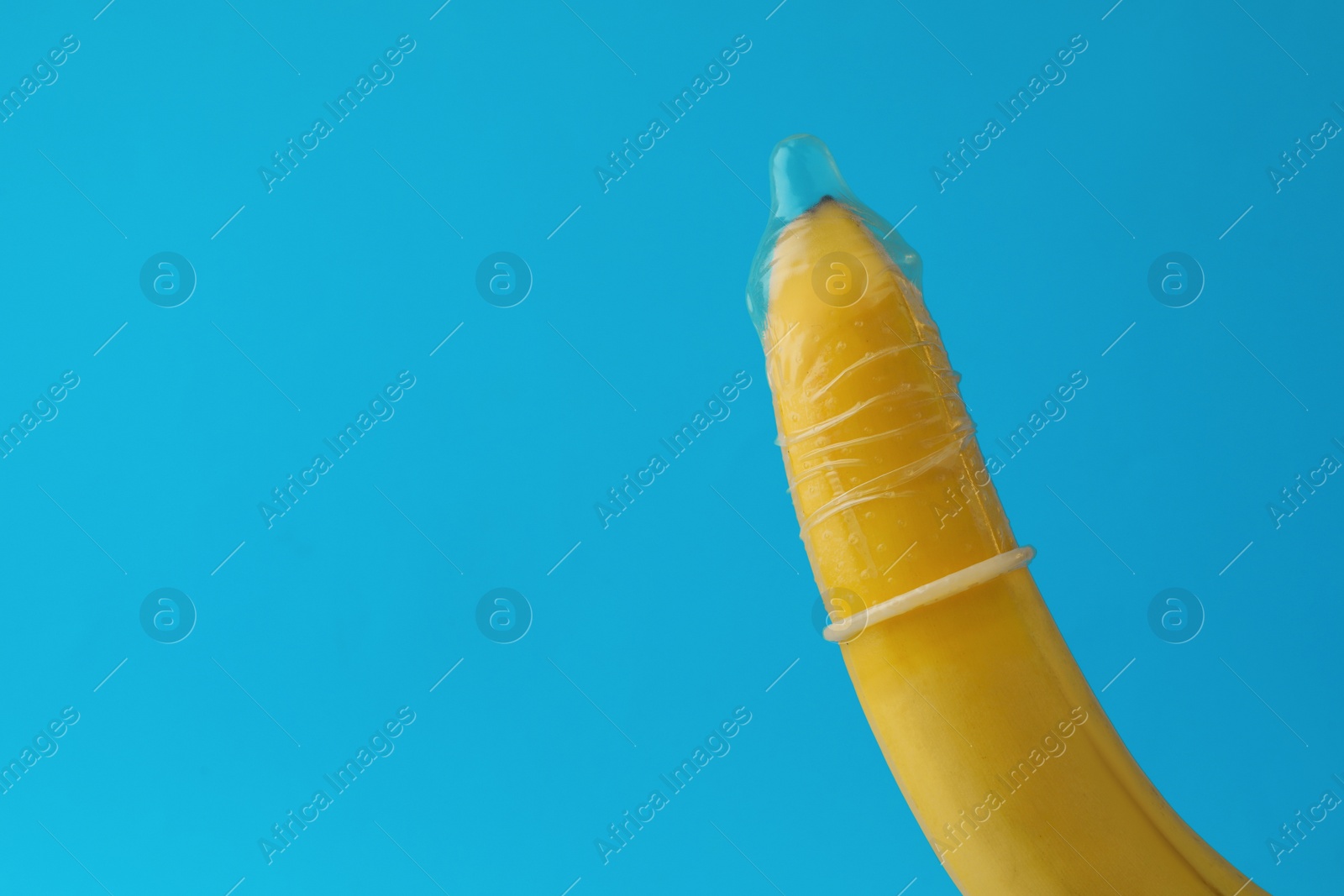 Photo of Banana with condom on light blue background, closeup and space for text. Safe sex concept