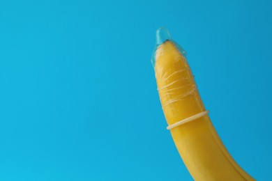 Photo of Banana with condom on light blue background, closeup and space for text. Safe sex concept
