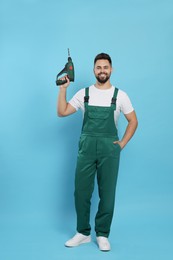 Photo of Young worker in uniform with power drill on light blue background