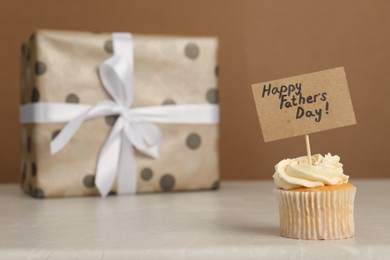 Happy Father's Day. Tasty cupcake with greetings and gift box on light marble table, closeup. Space for text