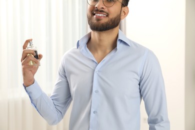 Photo of Young man spraying luxury perfume indoors, closeup