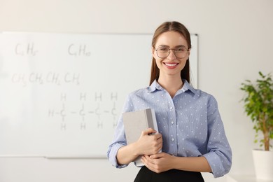 Portrait of young chemistry teacher near whiteboard in classroom. Space for text