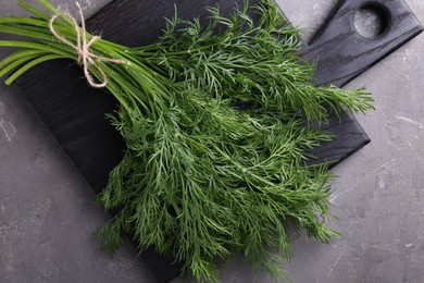 Photo of Board with bunch of fresh dill on grey textured table, top view