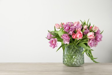 Photo of Beautiful bouquet of colorful tulip flowers on wooden table near light wall, space for text