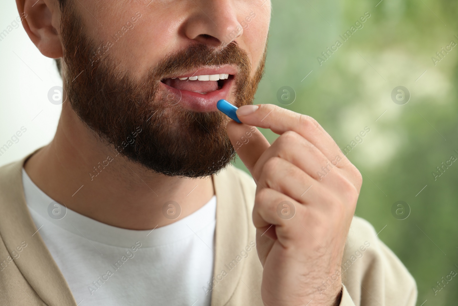 Photo of Closeup view of bearded man taking pill on blurred background