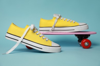 Photo of Pair of yellow classic old school sneakers and skateboard on light blue background
