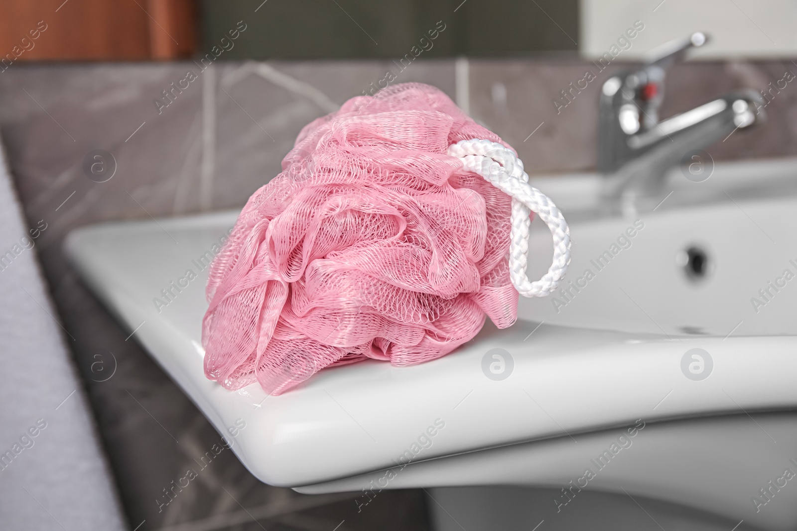 Photo of Pink shower puff on washbasin in bathroom, closeup