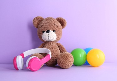 Photo of Baby songs. Toy bear, headphones and balls on violet background