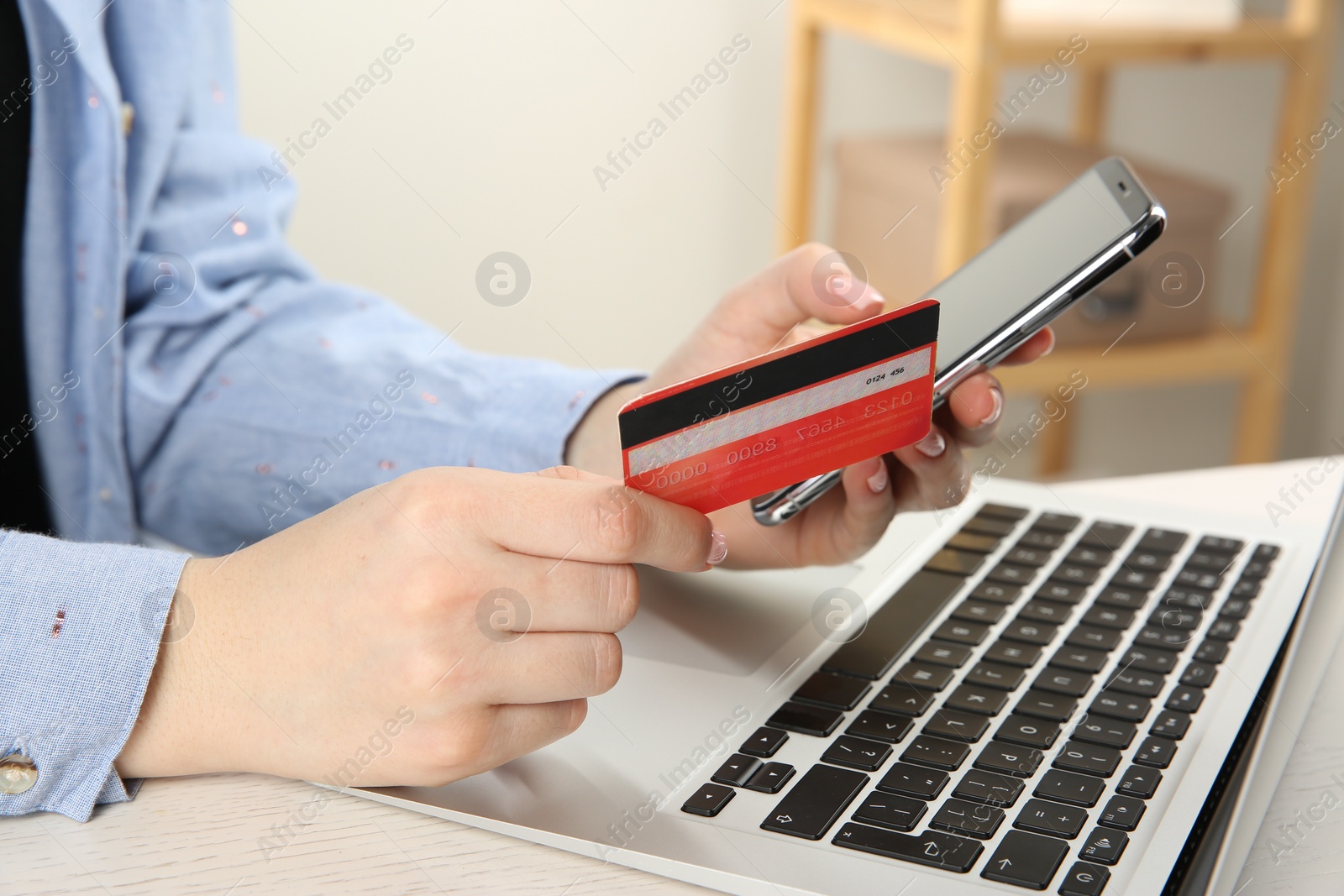 Photo of Online payment. Woman using credit card and smartphone near laptop at white wooden table indoors, closeup