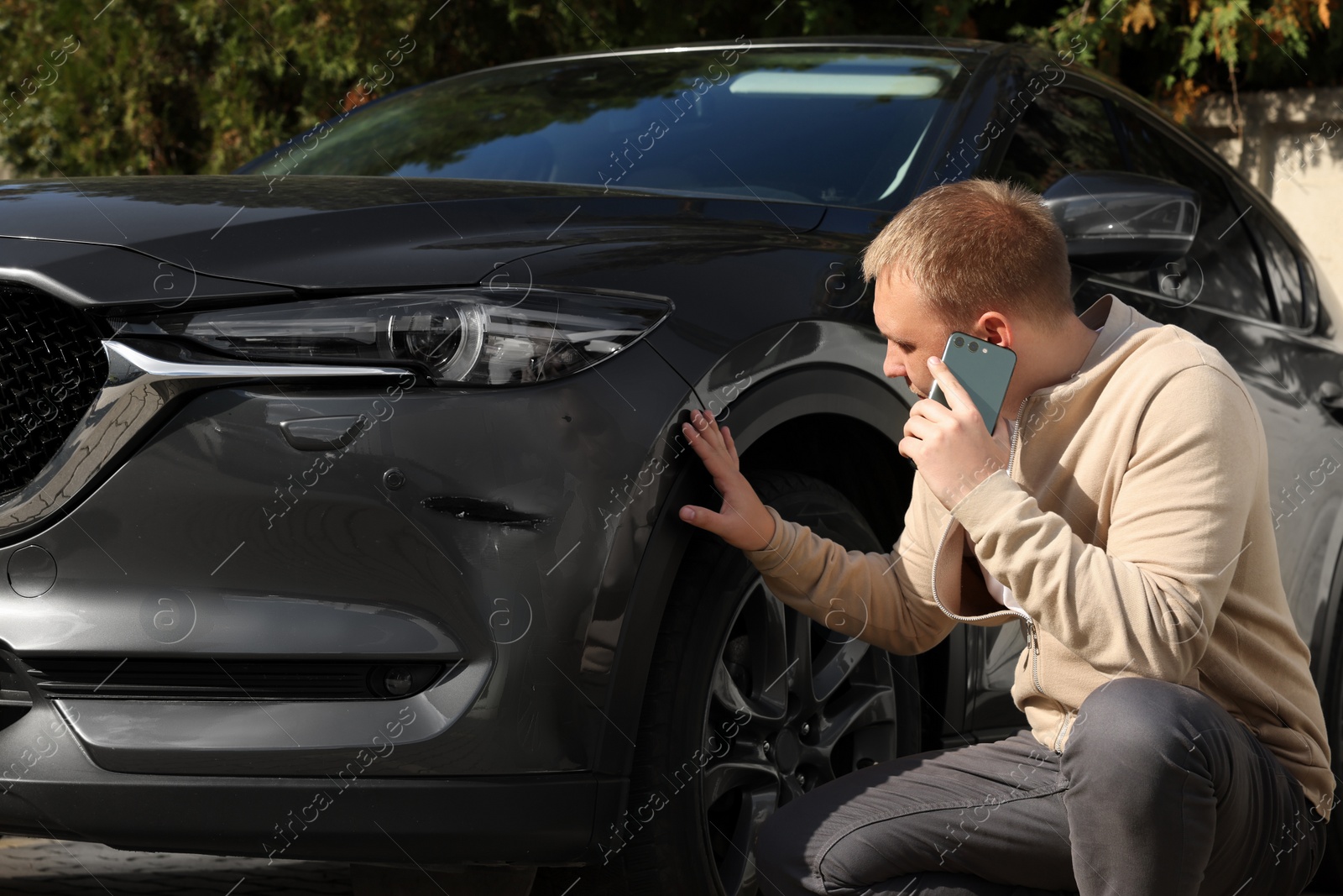 Photo of Man talking on phone near car with scratch outdoors