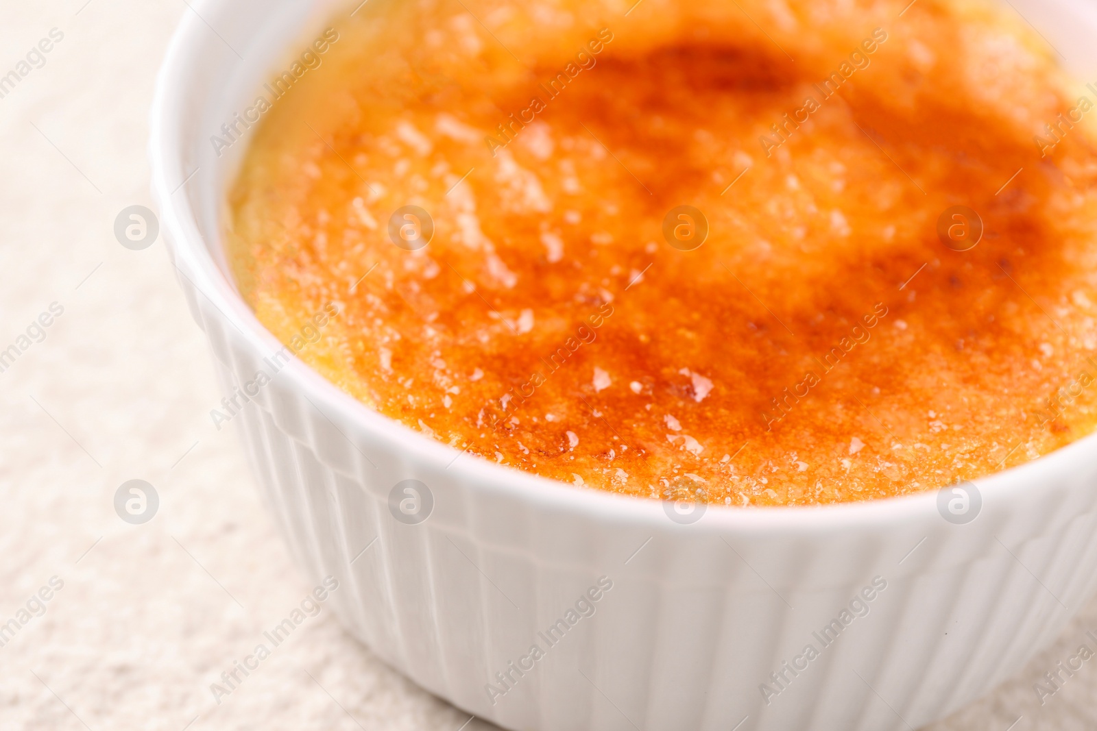 Photo of Delicious creme brulee in bowl on light textured table, closeup