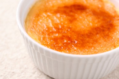 Delicious creme brulee in bowl on light textured table, closeup