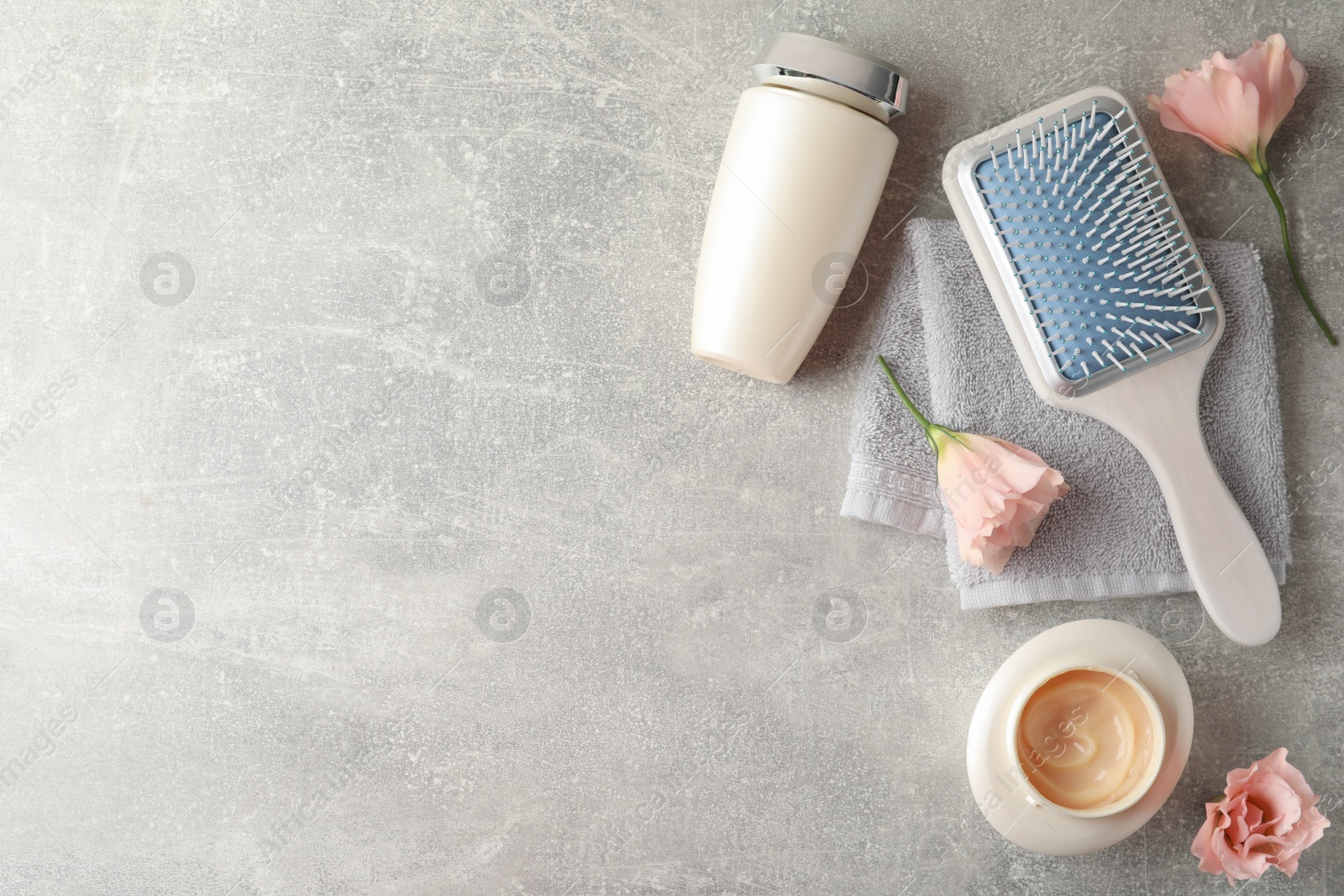 Photo of Hair care cosmetic products, brush and flowers on light grey table, flat lay. Space for text