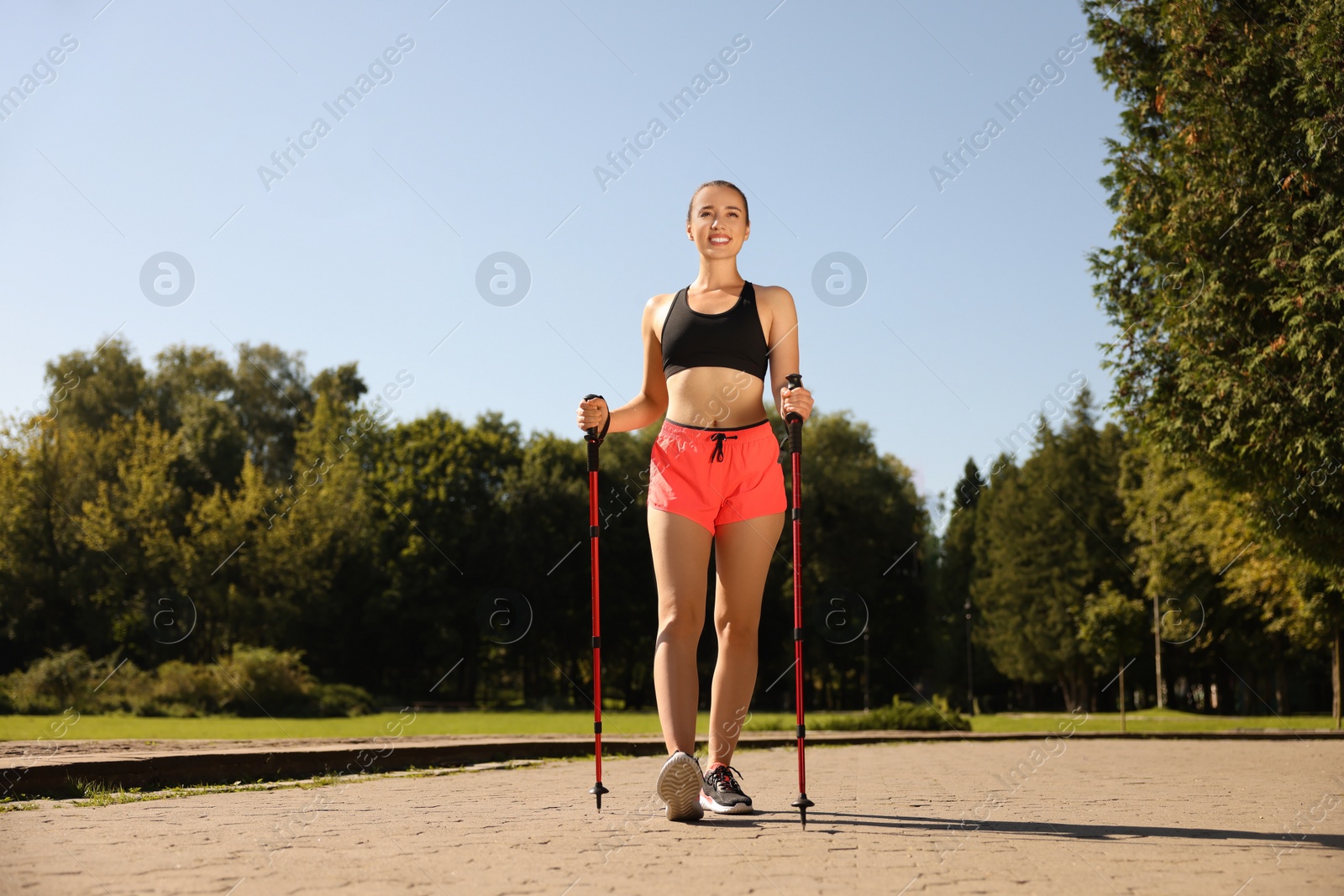 Photo of Happy woman practicing Nordic walking with poles in park on sunny day