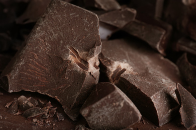 Photo of Pieces of dark chocolate on brown table, closeup