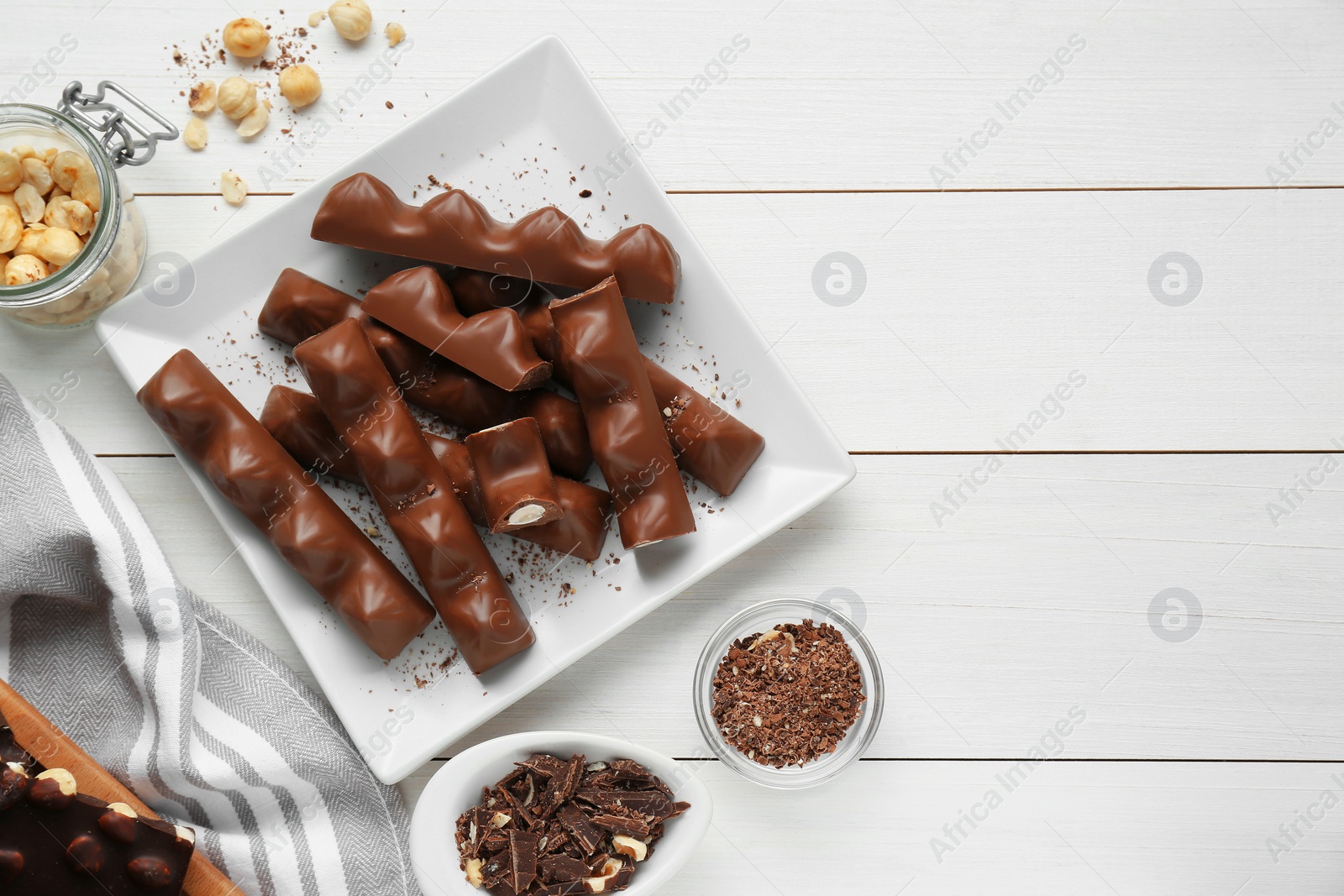 Photo of Tasty chocolate bars with nuts on white wooden table, flat lay. Space for text