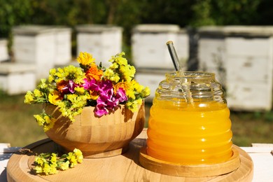 Photo of Delicious fresh honey and beautiful flowers on wooden board in apiary