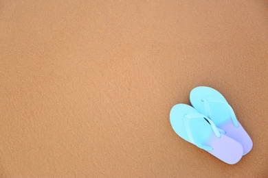 Photo of Stylish flip flops on sand, top view with space for text. Beach accessories