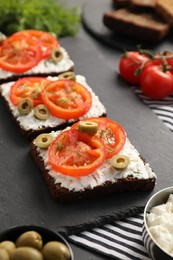 Photo of Delicious ricotta bruschettas with sliced tomatoes, olives and greens on black table, closeup