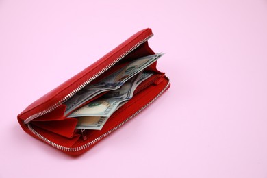 Stylish red leather purse with dollar banknotes on pink background, space for text
