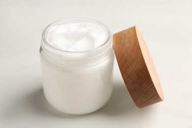 Photo of Glass jar of face cream on white marble table, closeup