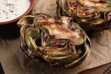 Photo of Tasty grilled artichoke and sauce on table, closeup