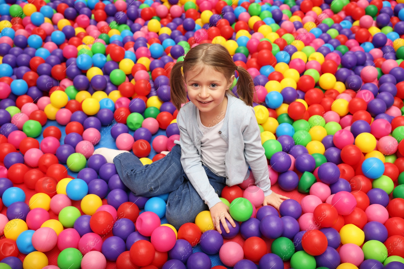 Photo of Happy little girl sitting on colorful balls in ball pit