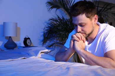 Photo of Handsome man saying bedtime prayer in dark room at night. Space for text