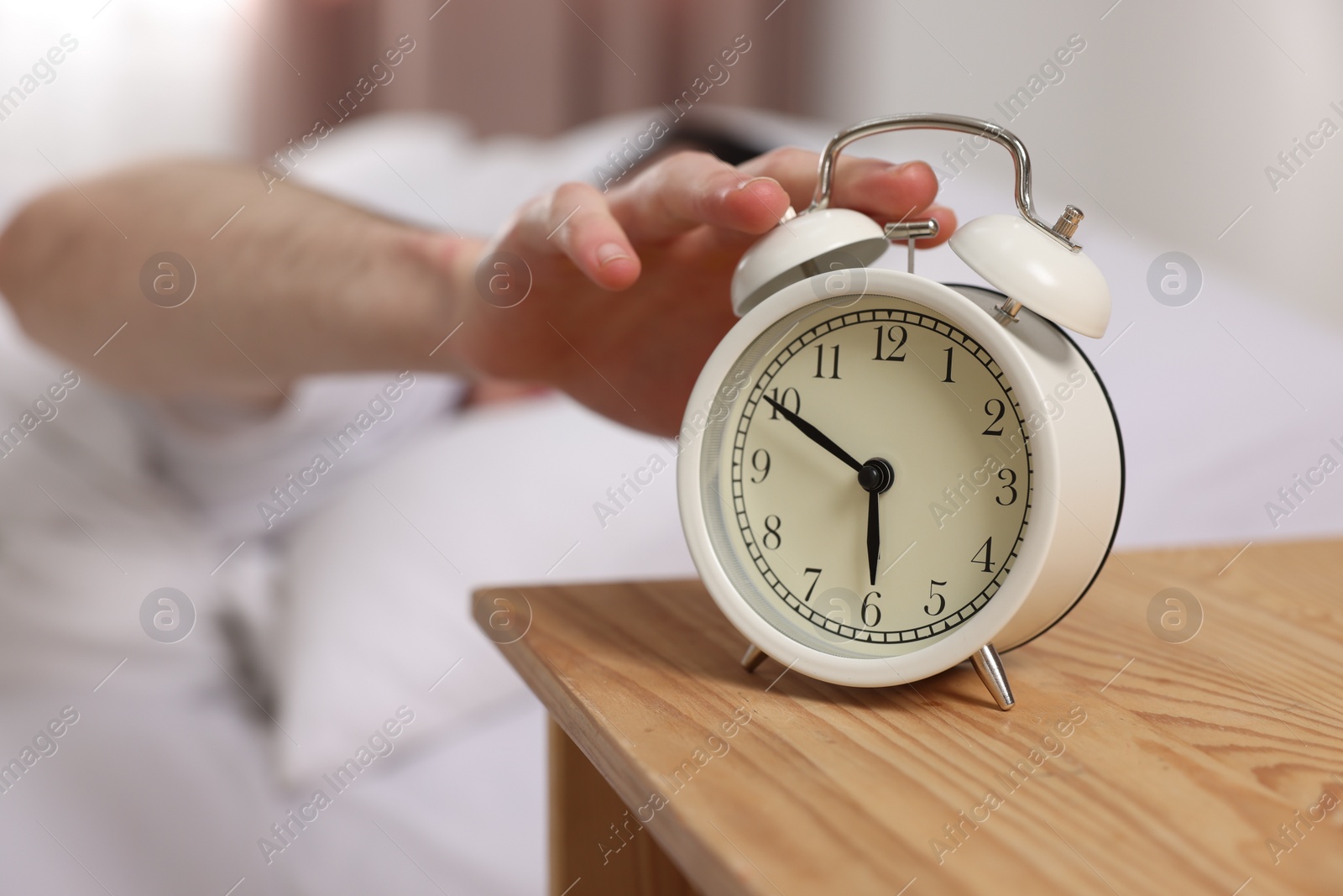 Photo of Man turning off alarm clock in bedroom, focus on hand