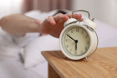 Man turning off alarm clock in bedroom, focus on hand