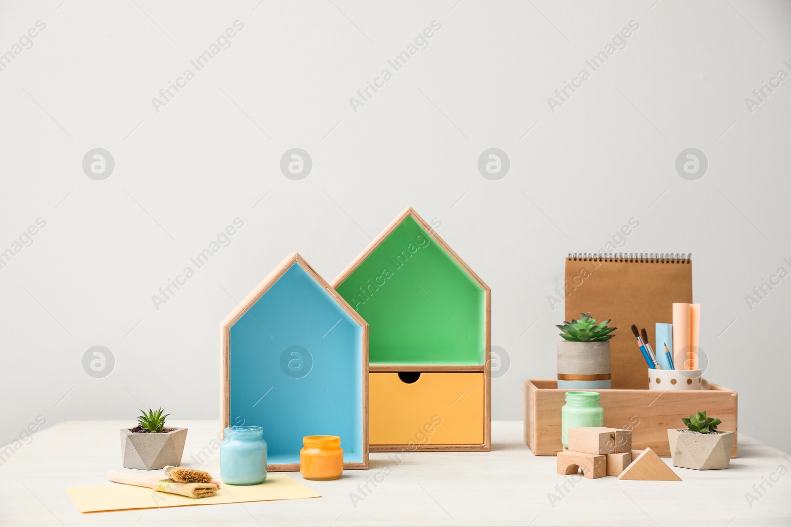 Photo of Composition with house shaped shelves and jars of paints on white table. Interior elements