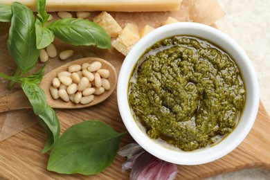 Photo of Tasty pesto sauce in bowl, basil, pine nuts, garlic and cheese on table, top view