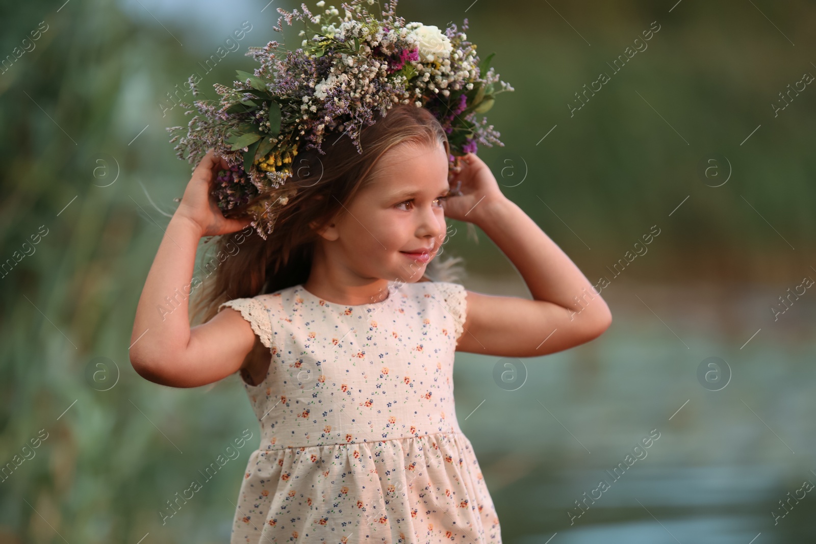 Photo of Cute little girl wearing wreath made of beautiful flowers outdoors