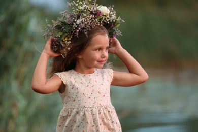 Photo of Cute little girl wearing wreath made of beautiful flowers outdoors