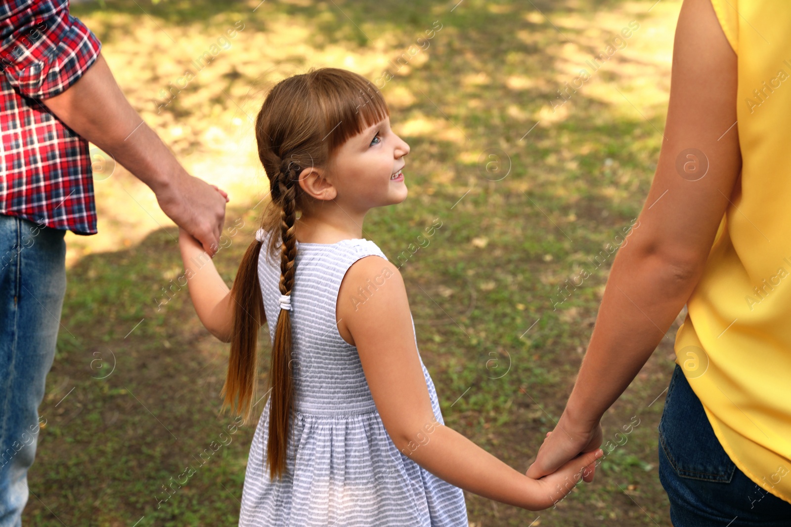 Photo of Little girl and her parents holding hands outdoors. Family weekend