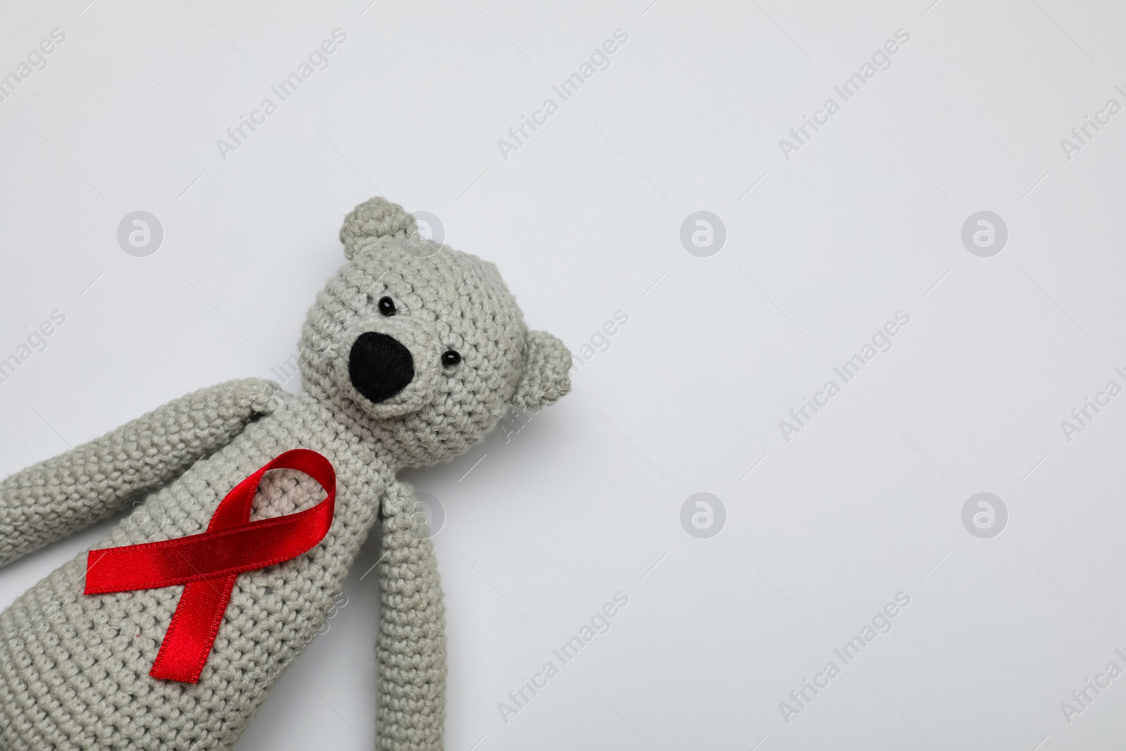 Photo of Cute knitted toy bear with red ribbon on light grey background, top view and space for text. AIDS disease awareness