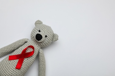 Cute knitted toy bear with red ribbon on light grey background, top view and space for text. AIDS disease awareness