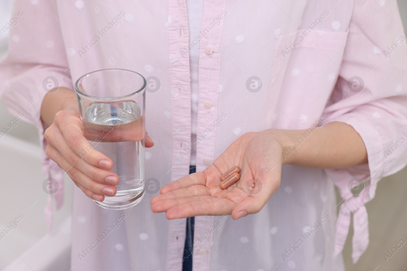 Photo of Woman with vitamin pills and glass of water indoors, closeup