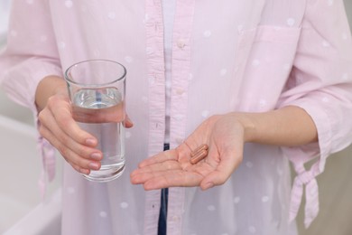 Woman with vitamin pills and glass of water indoors, closeup