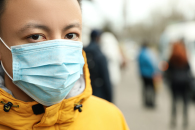 Photo of Asian man wearing medical mask on city street, closeup with view space for text. Virus outbreak