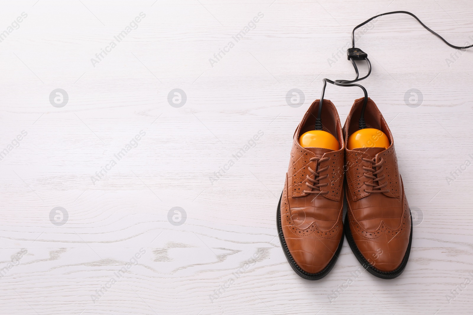 Photo of Shoes with electric dryer on white wooden background, space for text