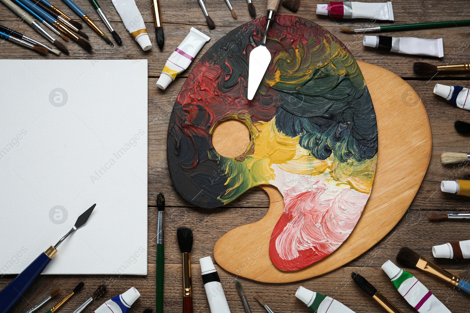 Photo of Blank canvas, brushes, paints and palette on wooden table, flat lay. space for text