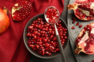 Photo of Tasty ripe pomegranates and grains on dark wooden table, flat lay