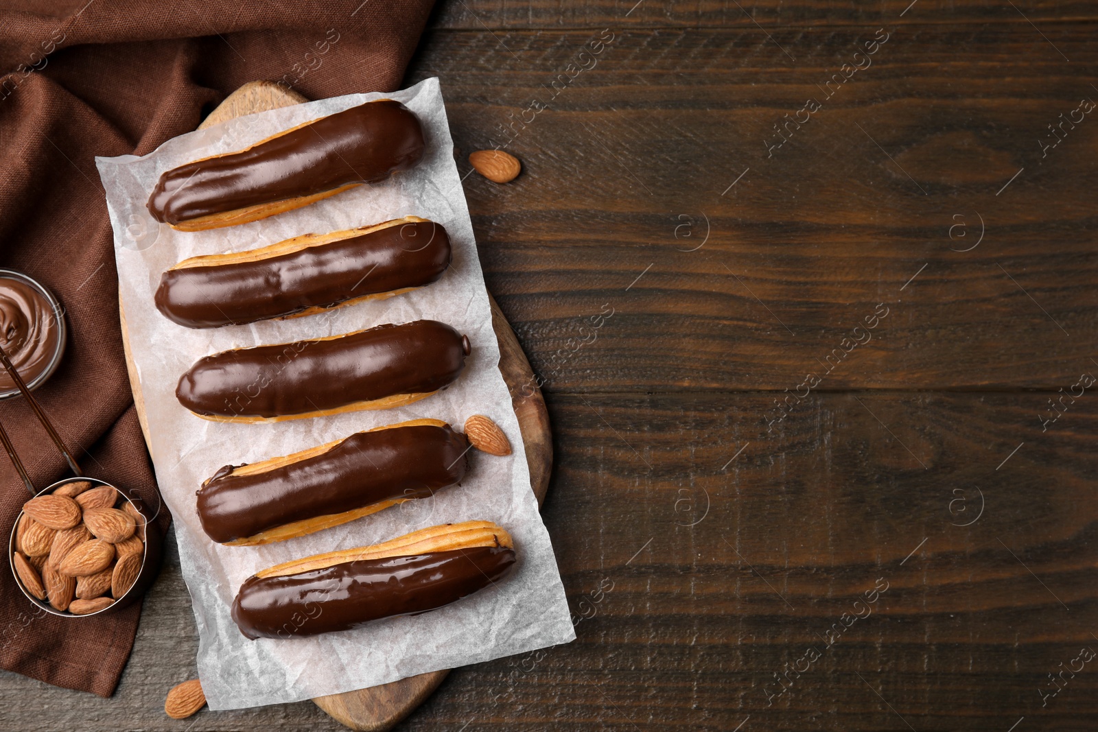 Photo of Delicious eclairs covered with chocolate and almonds on wooden table, flat lay. Space for text