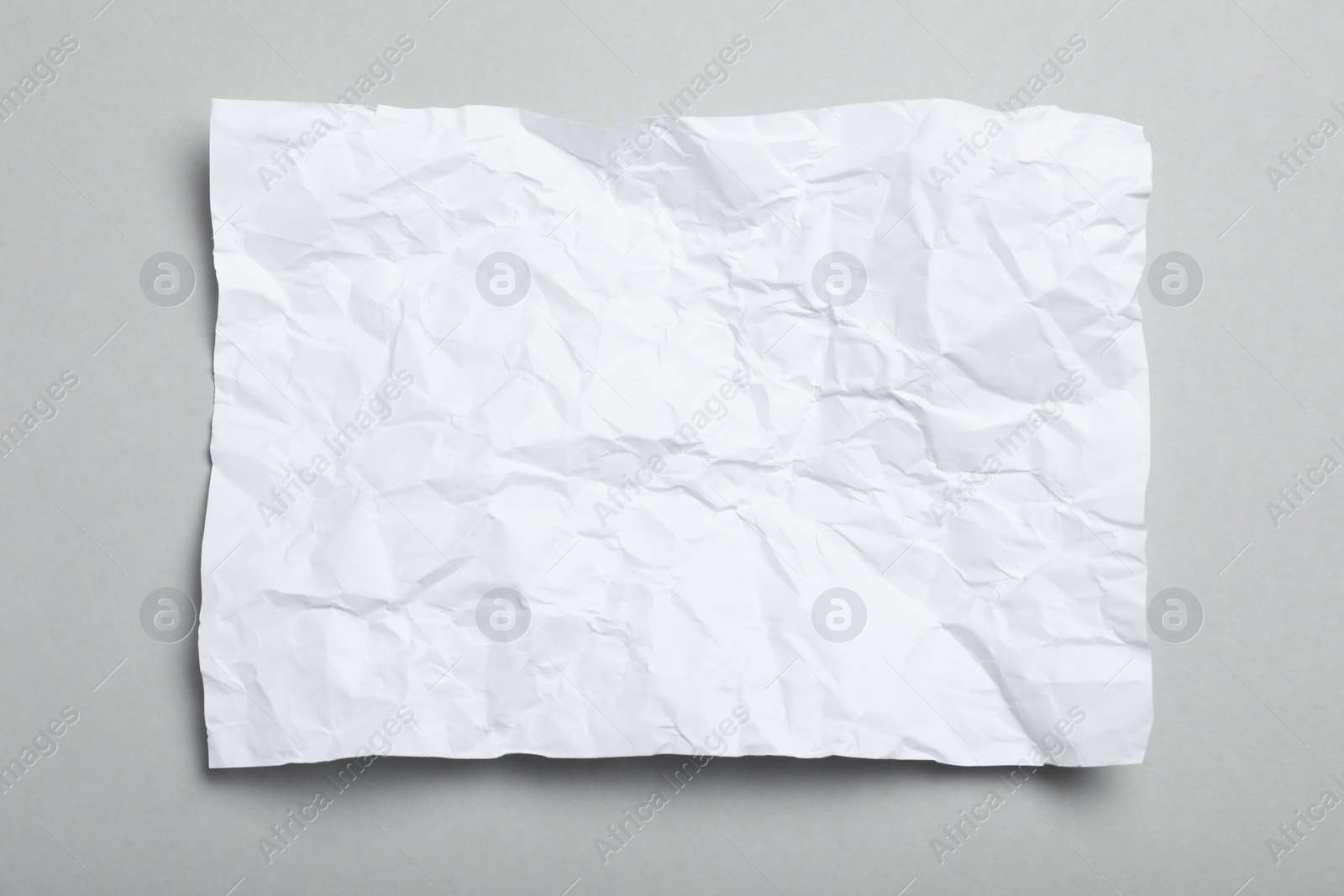 Photo of Sheet of white crumpled paper on grey background, top view