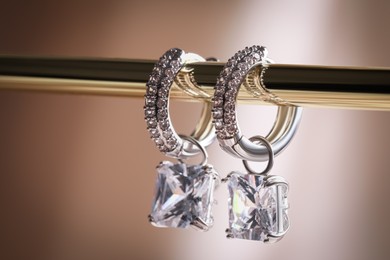 Photo of Elegant jewelry. Stylish presentation of luxury earrings hanging on golden holder, closeup