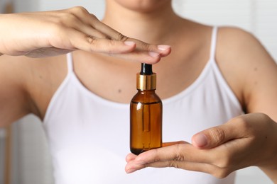 Woman with bottle of cosmetic serum on blurred background, closeup