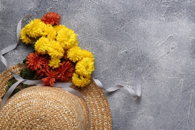 Flat lay composition with bright chrysanthemum flowers and wicker hat on grey textured table. Space for text